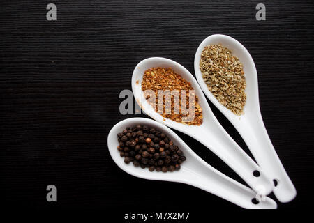 Black and red pepper, a set of spices in spoons. On a black wooden table Stock Photo
