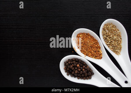 Black and red pepper, a set of spices in spoons. On a black wooden table Stock Photo