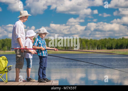 on a wooden pier the father teaches his sons to fish properly Stock Photo