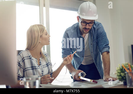 Young worried architect colleagues talking and analyzing blueprints while working on a new project at the office. Stock Photo