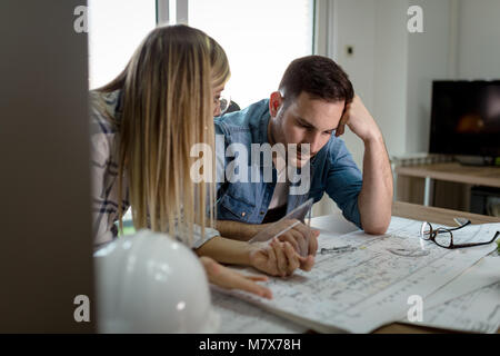 Young worried architect colleagues talking and analyzing blueprints while working on a new project at the office. Stock Photo