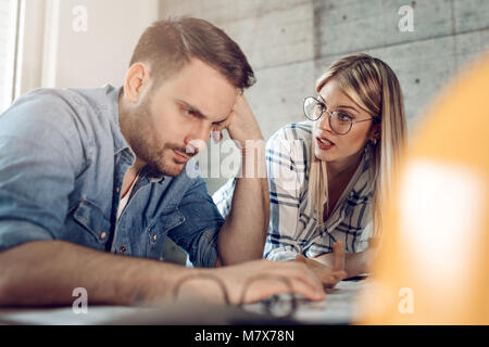 Young worried architect colleagues talking and analyzing blueprints while working on a new project at the office. Stock Photo