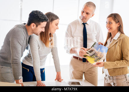Young couple consult with two real estate agents about buying new house. Stock Photo