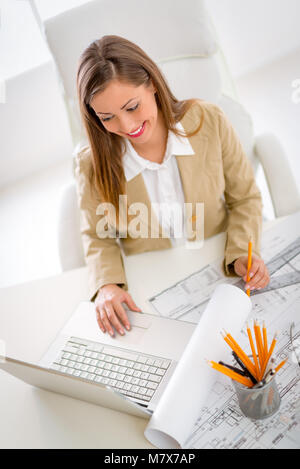 Smiling young businesswoman working on laptop at desk in office. Top view. Stock Photo