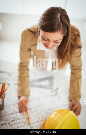 Young woman architect constructor analyzing blueprint at desk in office. Top view. Stock Photo
