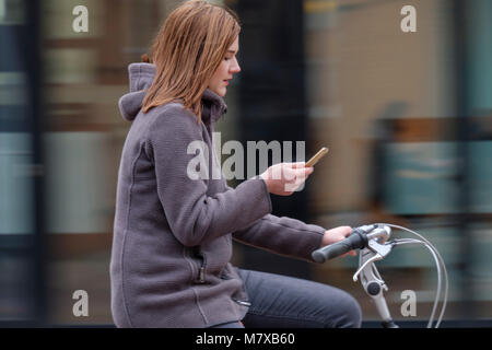 Young woman getting distracted by his smartphone while riding his bicycle around the city Stock Photo