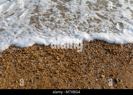 Fine shingle and sand with surf in the top half of the frame on a sunny day in early spring, Bexhill-on-Sea beach Stock Photo