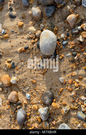 A soft grey pebble on sand with other pebbles and small stones scattered around. From a beach in Bexhill-on-Sea, East Sussex, England Stock Photo