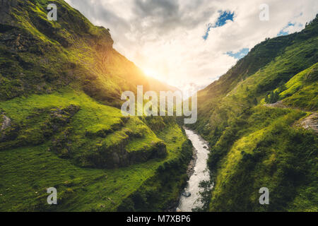 View with amazing mountains covered green grass, river, meadows and forest, blue sky with clouds, sun in autumn in Nepal at sunset. Mountain valley at Stock Photo