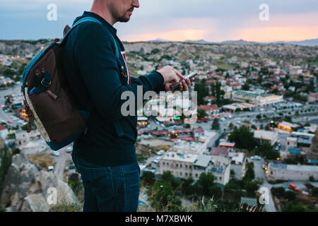 A tourist with a backpack on the background of the setting sun looks at the phone for geolocation and a mobile application and is going to call. Eveni Stock Photo