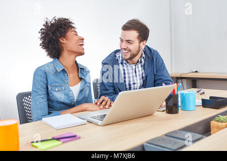 Two students have fun together at the laptop computer in the business start-up Stock Photo