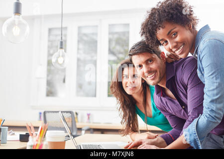 Three students as friends at the laptop. Computers form an office community Stock Photo