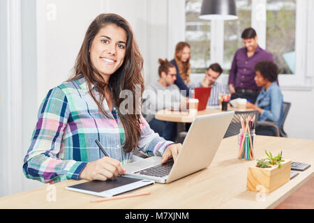 Young business woman as a creative graphic artist draws with pen on graphics tablet Stock Photo