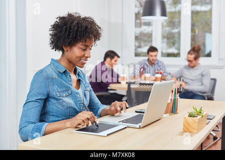 Young woman as graphic artist draws with pen on graphics tablet in coworking business Stock Photo