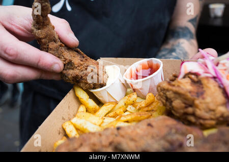 Fried chicken and chips with coleslaw, dipped in mayonnaise with ketchup by man with tattoos.  Hipster street food. Stock Photo