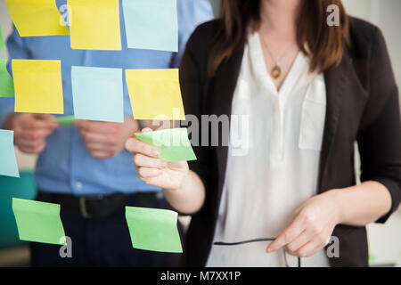 Midsection Of Businesswoman Sticking Note On Glass By Executive Stock Photo