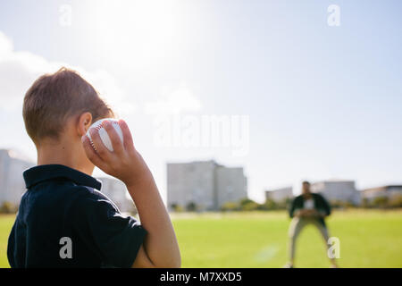 Rear view close up of a boy throwing baseball at a man in a ground. Boy playing with a baseball along with his father. Stock Photo