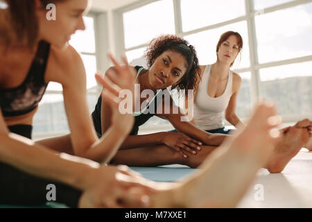 Young female relaxing and talking after workout session. Female friends during yoga class break at fitness center. Stock Photo