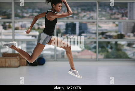 Female with slim figure running and jumping in fitness studio. Healthy african woman working out indoors. Stock Photo