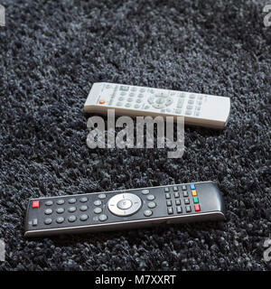Two remote controls are on wool carpet on a floor Stock Photo