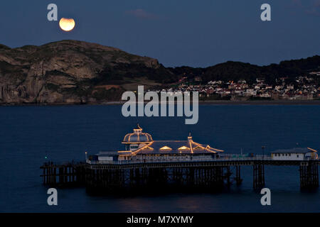 Partial lunar eclipse over the pier at Llandudno, North Wales coast Stock Photo