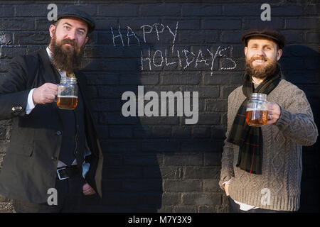 Holiday photo of two men drinking beer with Christmas greetings on the wall behind them. Stock Photo