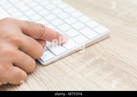 Close up hand with injury on finger using white computer keyboard on wooden background Stock Photo