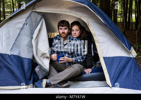 A couple sitting inside a tent with the man holding a cup of morning coffee. Stock Photo