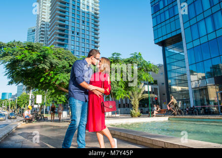 Portrait of a beautiful couple in bright clothes and sunglasses embracing, laughing during walk in the street with skyscrapers. Happiness, lifestyle a Stock Photo
