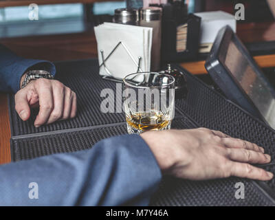 The man in a suit sits at a bar counter with a whisky glass Stock Photo