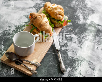 The fresh baked croissants with butter, a salty salmon and leaves of arugula on a chopping board on a wooden table. Breakfast concept Stock Photo