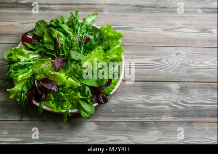 Leaves of fresh lettuce, arugula, spinach and beet sprouts in a plate on a wooden background. Stock Photo