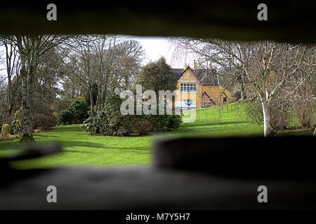 View through hole of house and gardens in the distance through a hole in the wall. Stock Photo