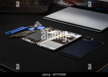 Workplace of the repairman with telephone and special purpose tools. The disassembled phone with tools on a black table Stock Photo