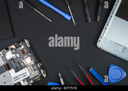 Details of the cell phone and special purpose tools of the master around on the black desktop with a blank space at center in flatlay style. Repair of Stock Photo