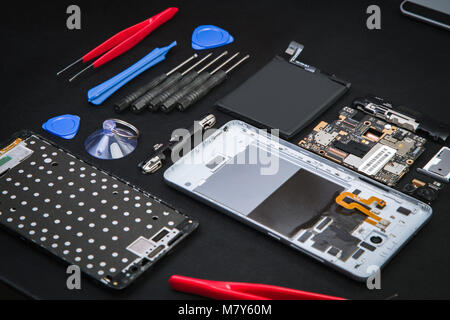 Repairman workplace with disassembled smartphone and special purpose tools. Broken cell phone diagnostics at service center. Stock Photo