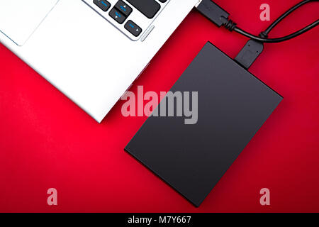 A portable hdd connected to a laptop on a red background, top view. The concept of data storage Stock Photo