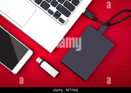 External hard drive connected to the laptop, USB flash drive and smartphone on a red background, flat lay. The concept of mobile technology Stock Photo