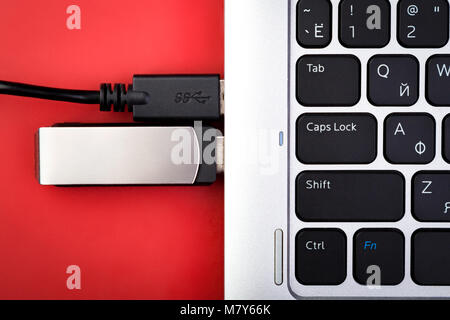 A flash drive and a wire from an external hard drive connected to a laptop on a red background. The concept of portable data storage Stock Photo