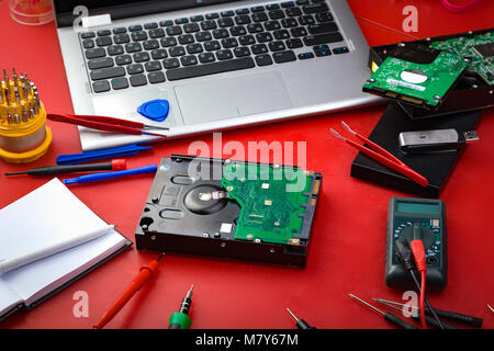 Hard disk, computer parts, laptop and special tools for repair on the red board. The concept of a repairman's workplace Stock Photo