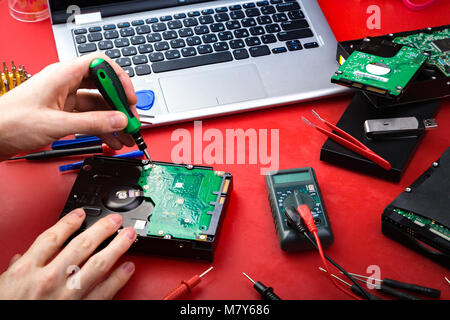 The process of repairing a hard drive by a repairman on a red table with special tools Stock Photo