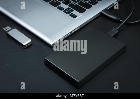 External hdd connected to the laptop and USB flash drive on a black background, top view. The concept of portable data storage Stock Photo