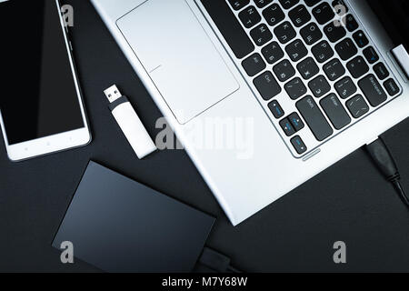 External hdd connected to the laptop, USB flash drive and smartphone on a black background, top view. The concept of portable data storage Stock Photo