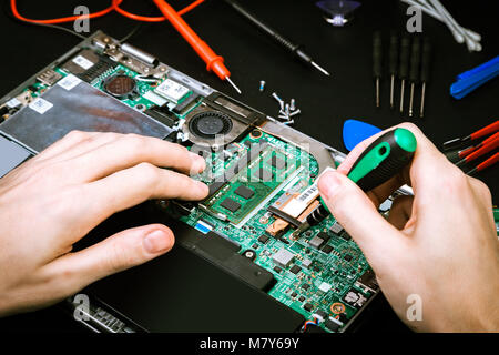 The process of repairing the disassembled laptop with special tools on a black board. Workplace of computer repair specialist Stock Photo