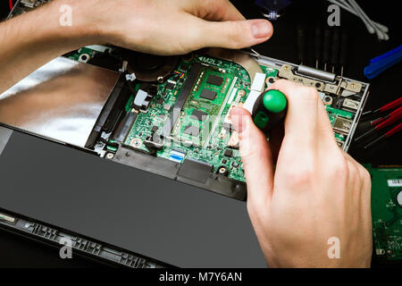 Repair a broken laptop with details and special tools on a black desk. Work process of the repairman. The pieces of computer Stock Photo