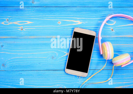 Top view smartphone and new modern pink music headphone on blue wooden plank background. With space for text or design Stock Photo