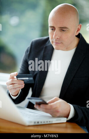 Man looking at laptop holding credit card Stock Photo