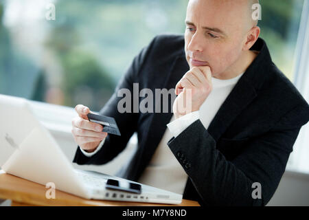 Man looking at laptop holding credit card Stock Photo