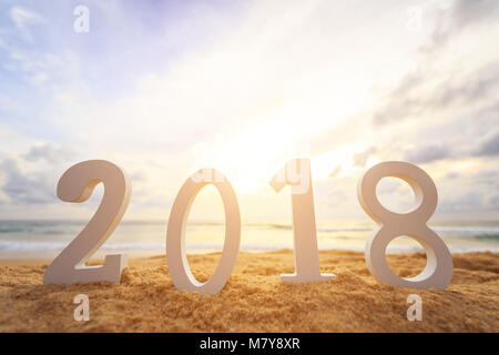 New year concept : Close up white wooden alphabet 2018 setup on the sunset beach. Warm tone color with lens flare. Stock Photo