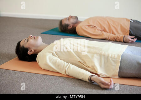 Two young people practising relaxation also called yoga nidra. Laying in shavasana on their backs, on their yoga mats in yoga class indoor in loose li Stock Photo